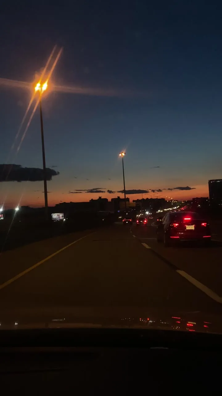 View ahead along a road at dusk with a glowing street lamp and an orange band of sky at the horizon.