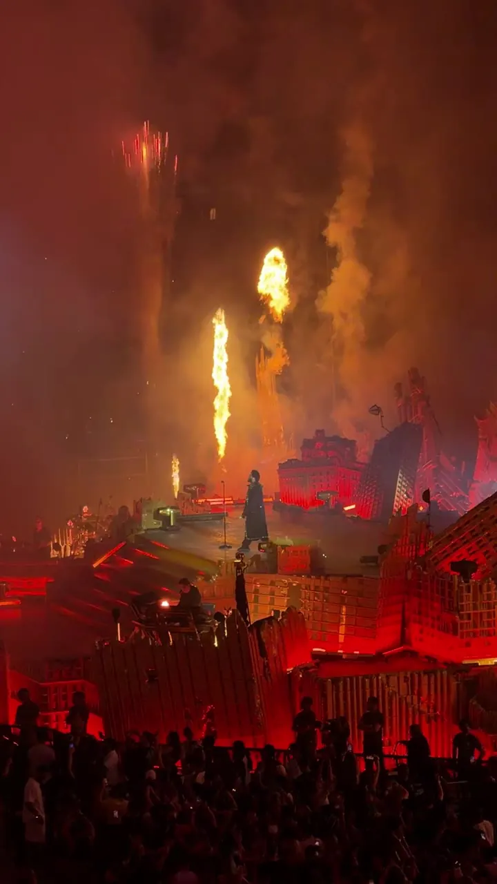 Stage lit in red with flames and smoke, with the silhouettes of a crowd in front.
