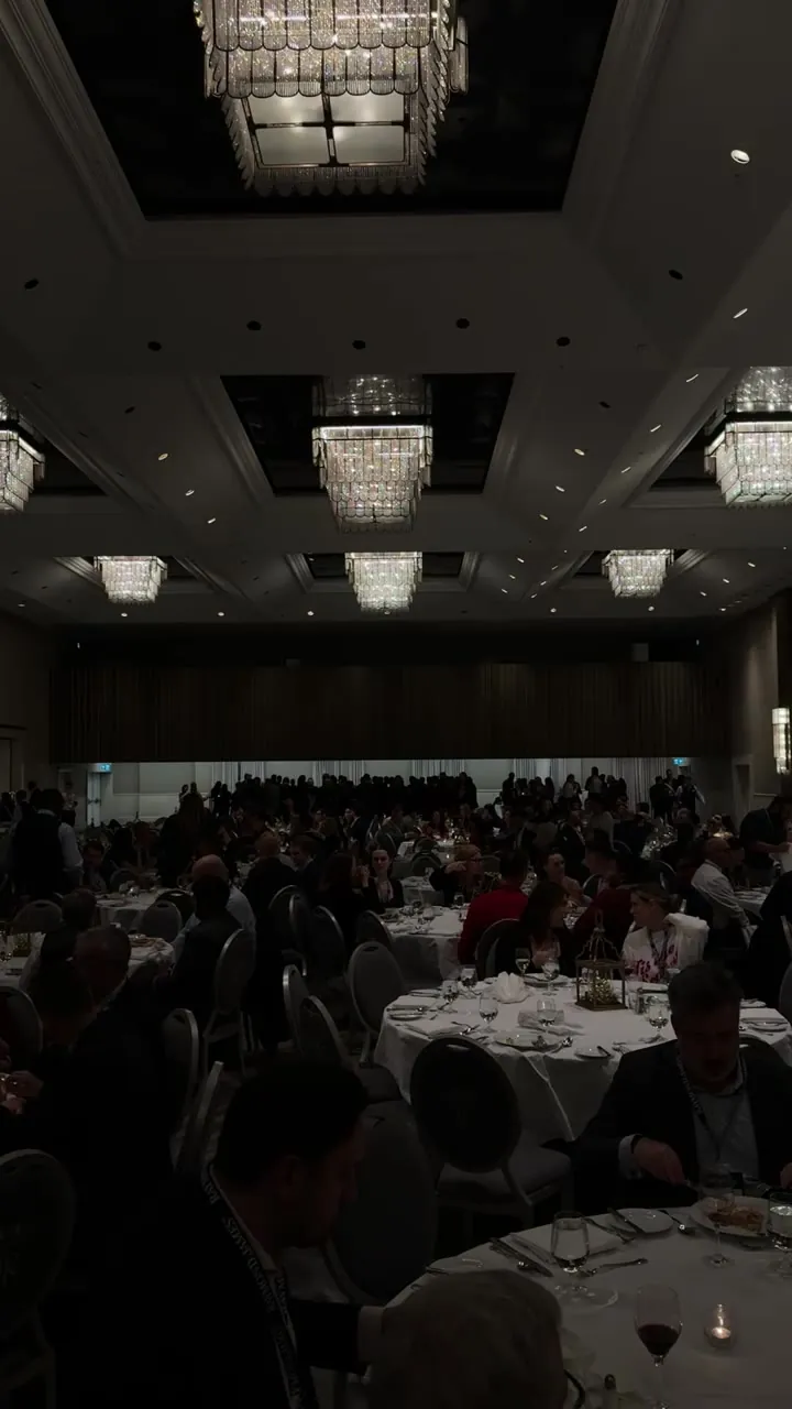 Large dim banquet hall with chandeliers and round tables of guests.