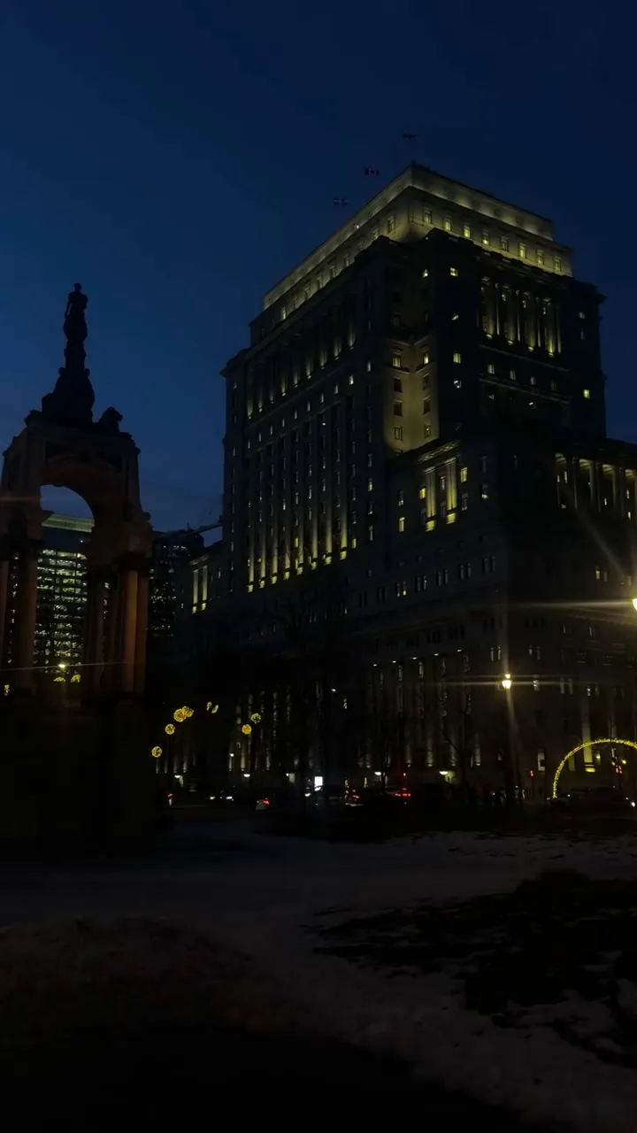 Tall lit office building at night against a dark blue sky.