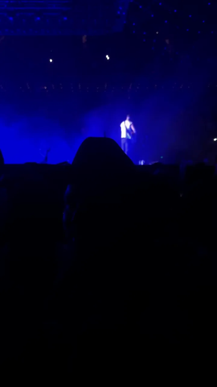 Performer on a stage lit in deep blue, with the audience in silhouette in front.