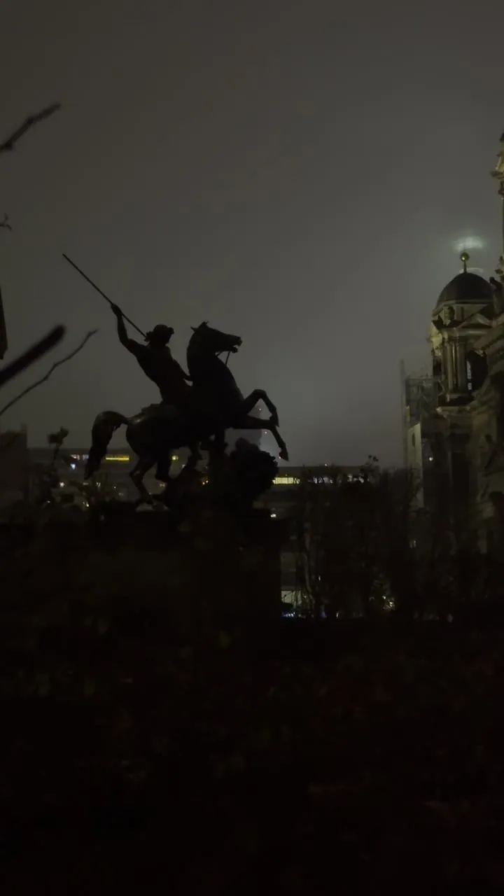 Large domed stone building and a statue in silhouette against an overcast night sky.