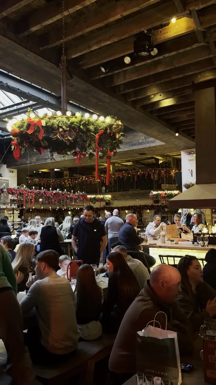 Busy indoor food market with a hanging wreath of lights and diners at tables.