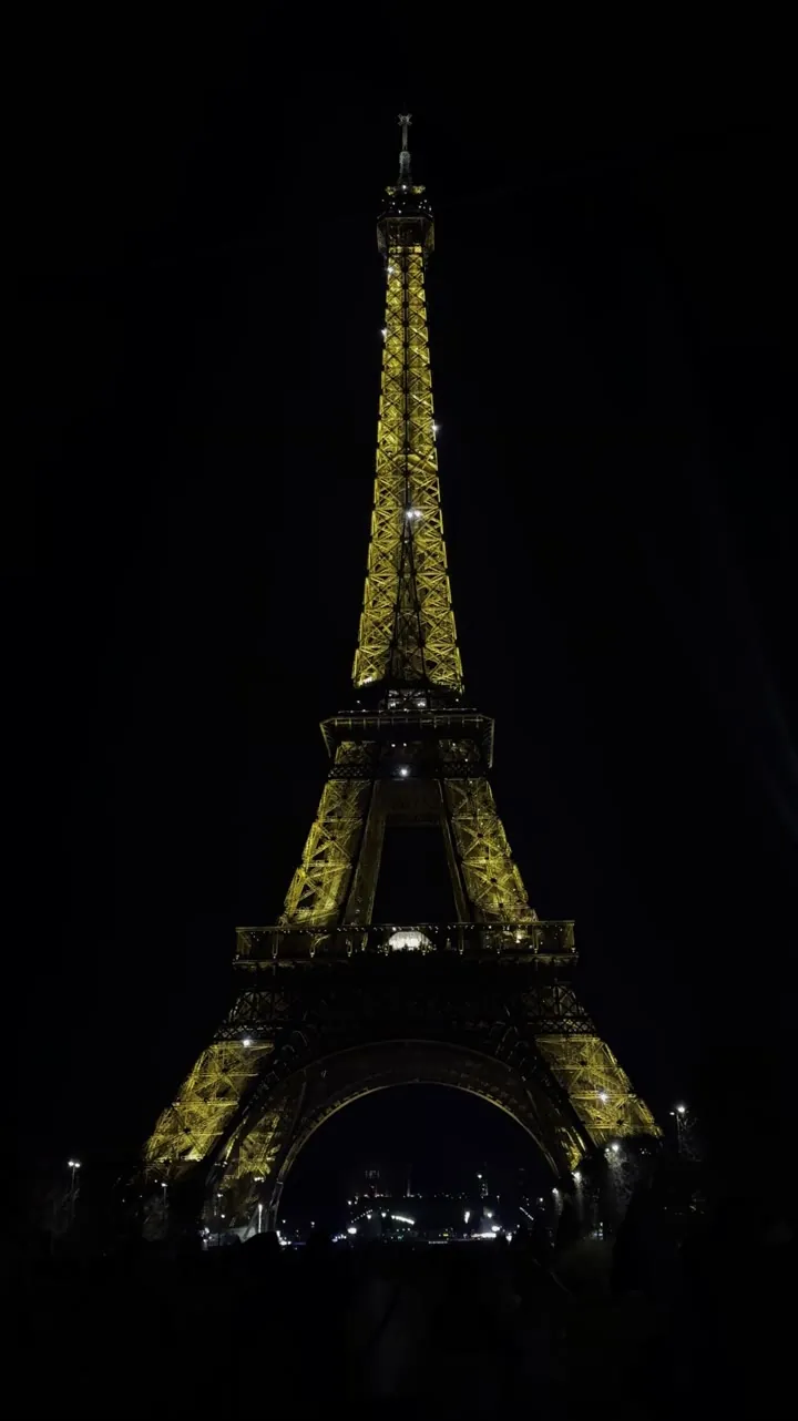 The Eiffel Tower lit in gold against a black night sky.