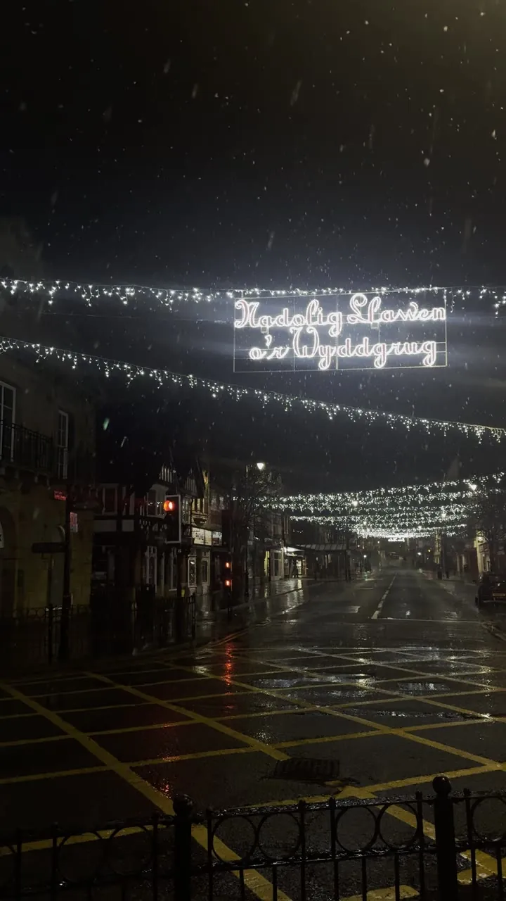 Night street with strings of lights and a lit sign across the road.