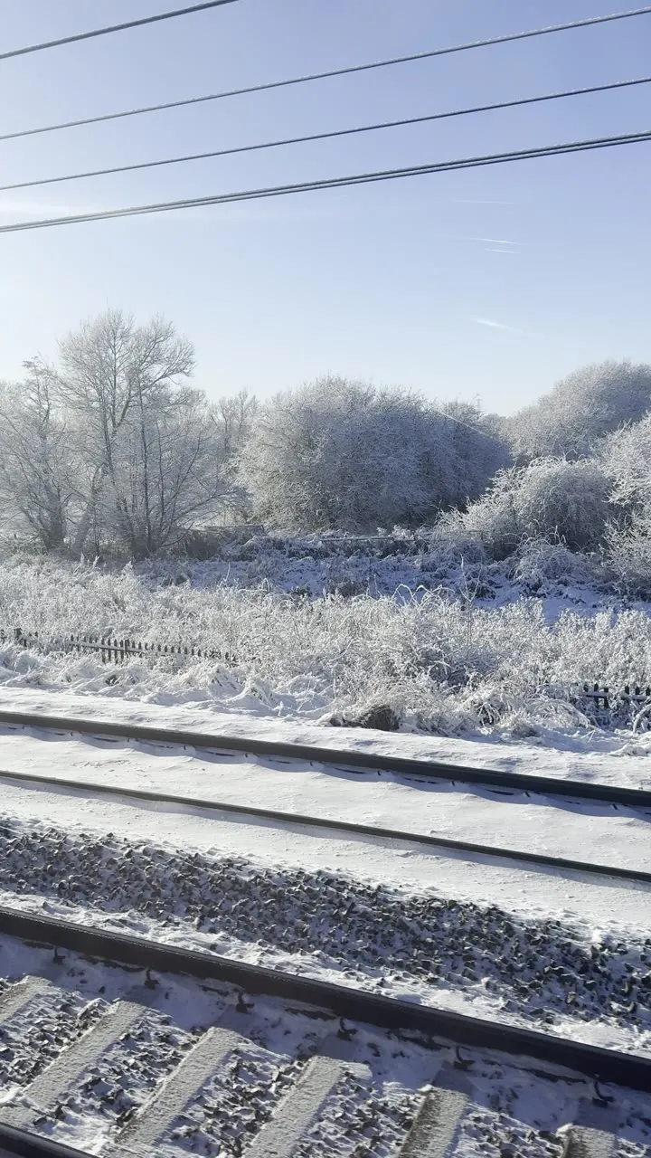 Frosted railway tracks and bare trees under a pale blue sky, with overhead wires.