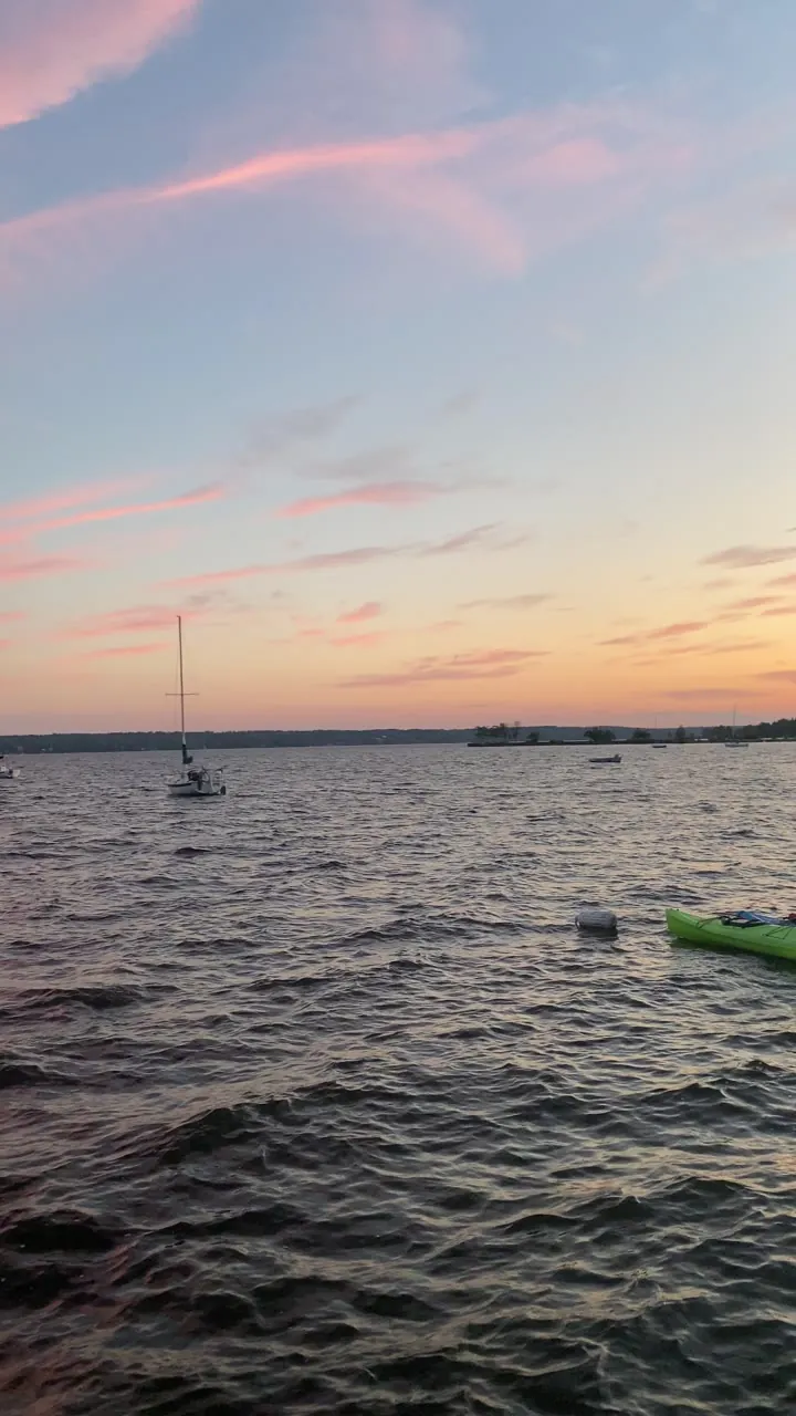 Lake at sunset with pink clouds and a small sailboat.