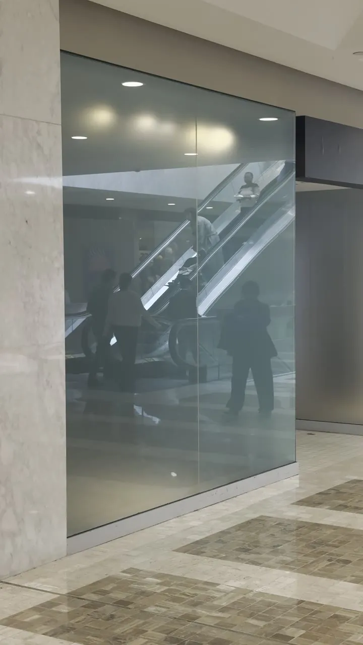 Glass-fronted corridor in a shopping centre with an escalator and a marble floor.