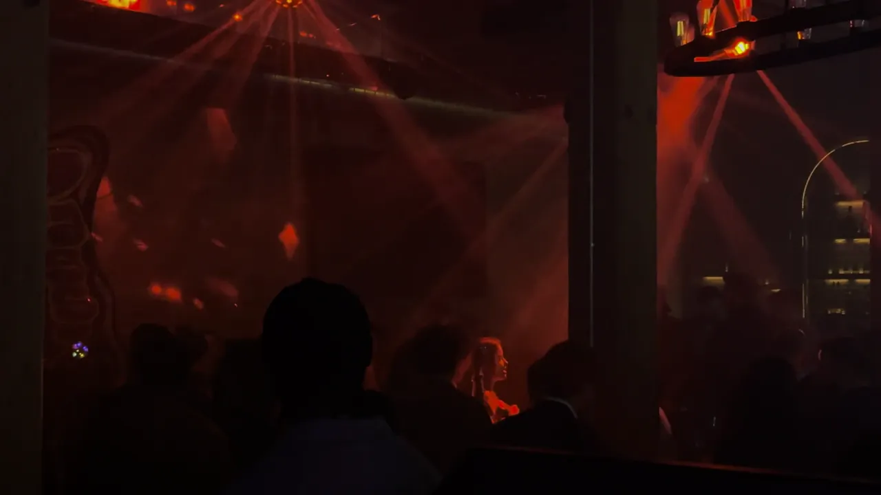 Dim venue lit by red beams of light, with silhouettes of people in the foreground.