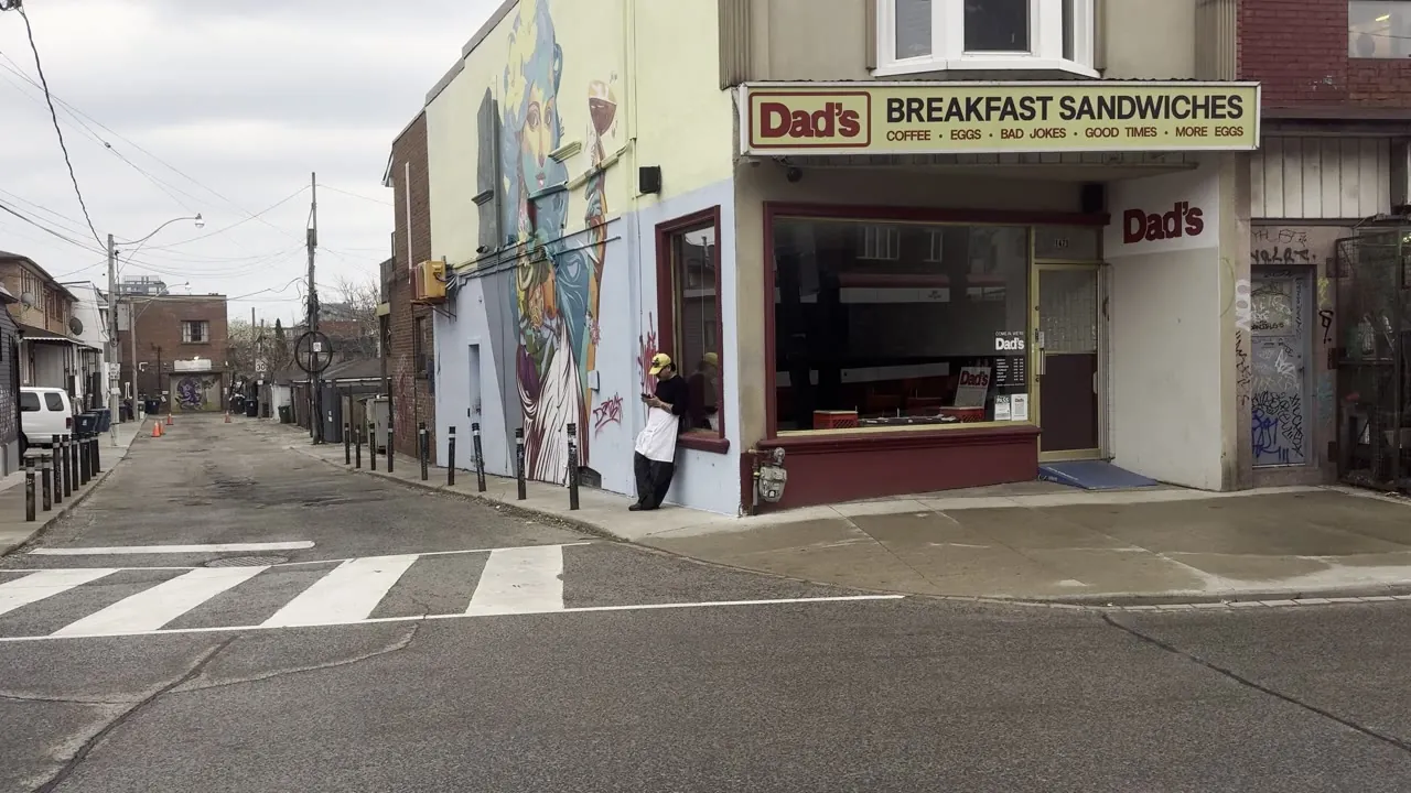 Quiet city street corner with a crosswalk and a breakfast sandwich shop.