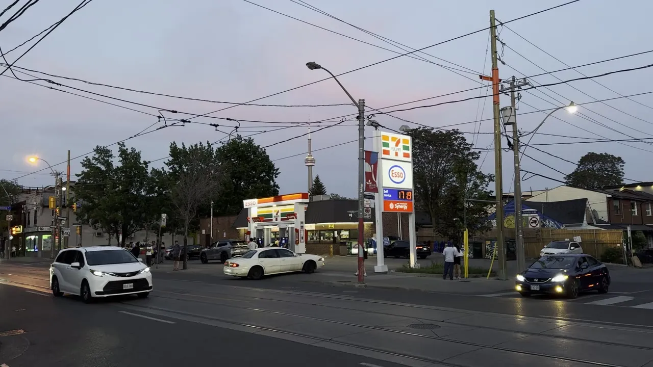 Street intersection at dusk with cars and a gas station sign.