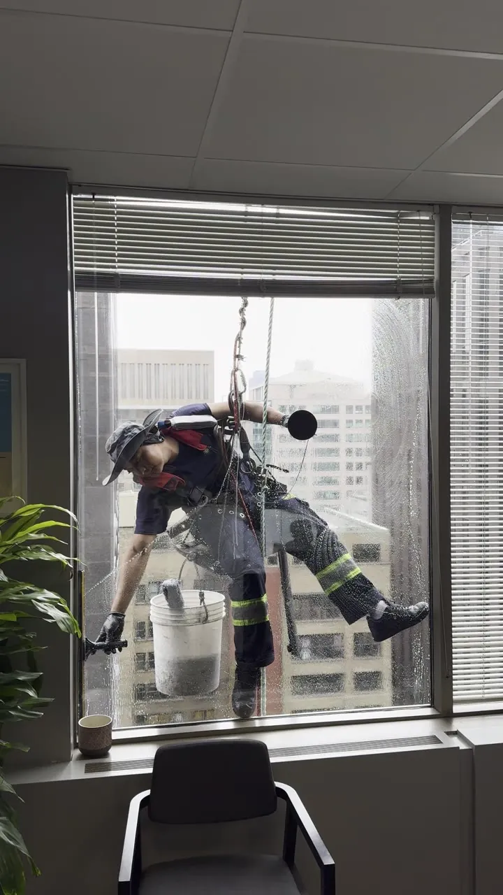 Window cleaner in a harness hanging outside an office window.