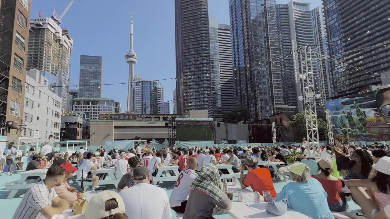People seated at long tables outdoors with downtown towers behind.