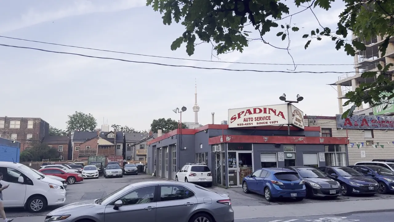 Auto service shop with a red and white sign and cars parked in a lot, with a tall tower on the skyline.
