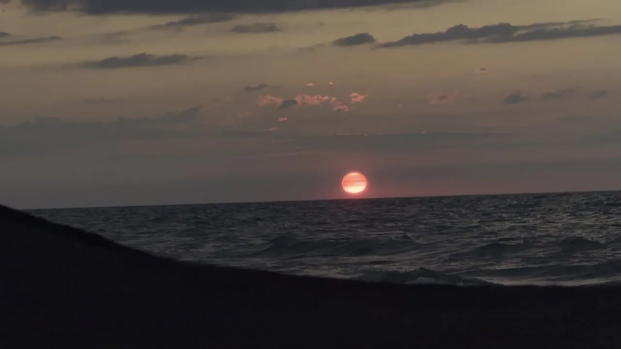 Low sun over dark water under a cloudy sky.