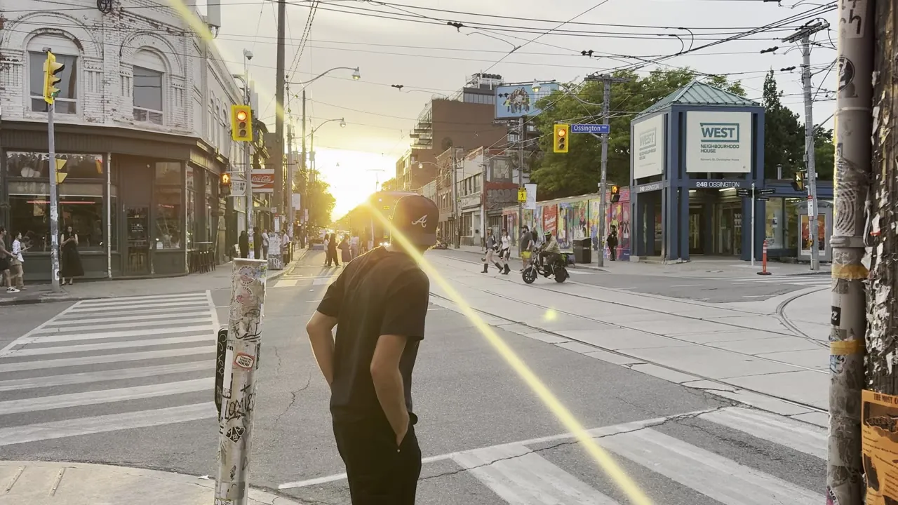 Street corner in low sun with a pedestrian in the foreground and a red city bus passing.