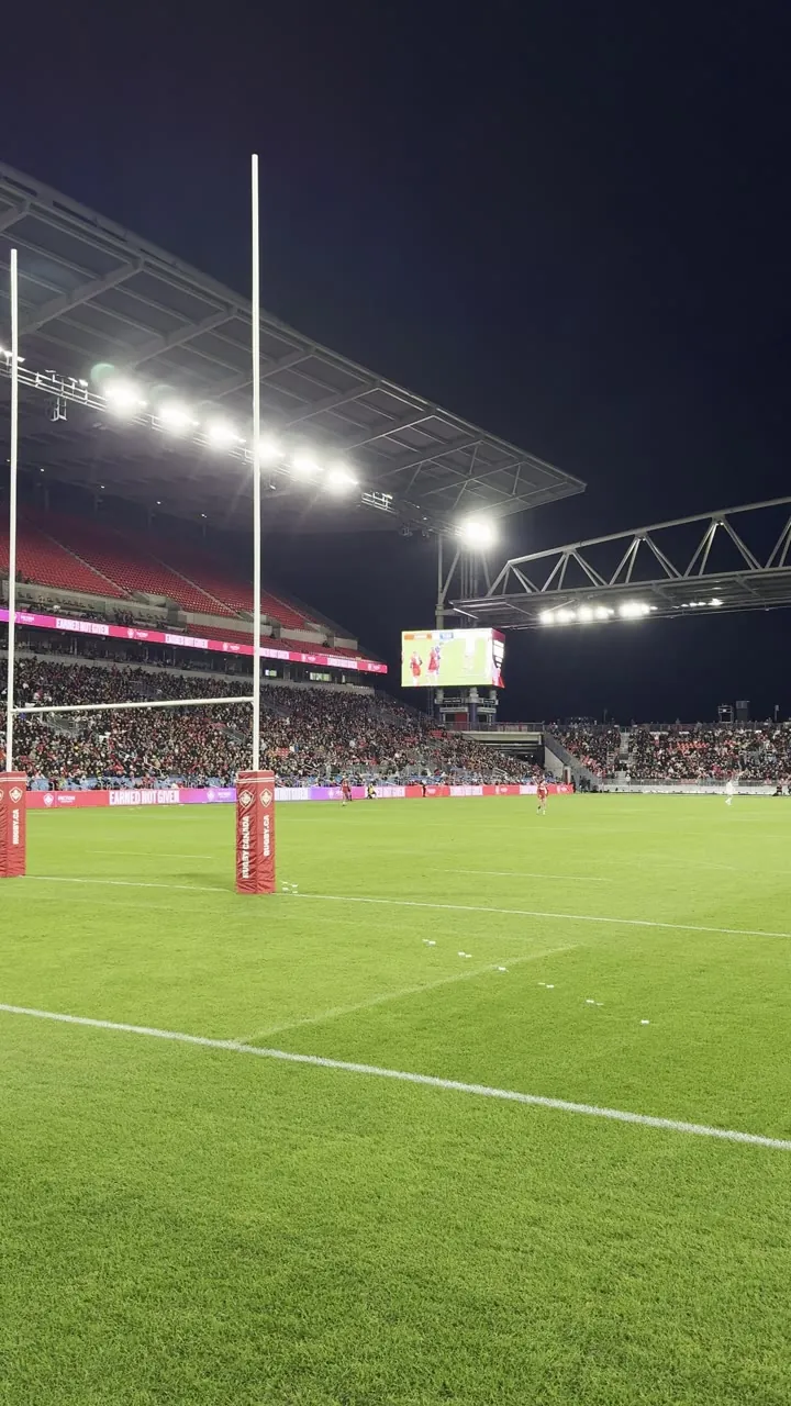 Stadium at night with goalposts, bright lights and a green pitch.