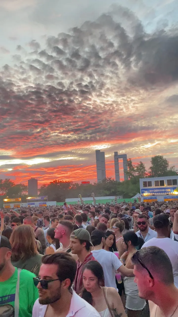 Crowd at an outdoor festival at sunset, with faces in the foreground and a colourful sky.