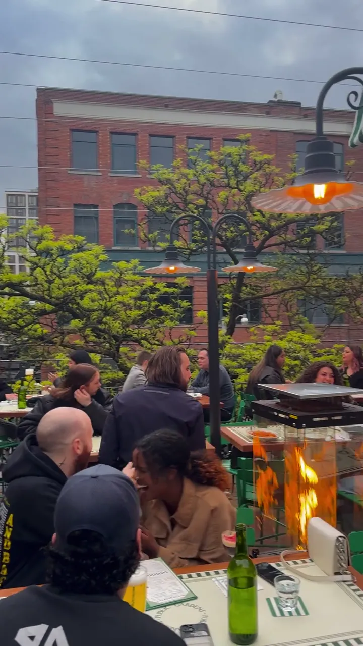 Restaurant patio with green and white striped awnings, brick buildings behind, and people seated at tables.