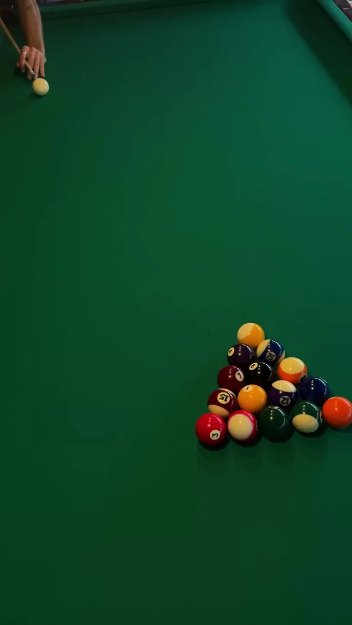 Pool table with balls racked in a triangle and a hand above.