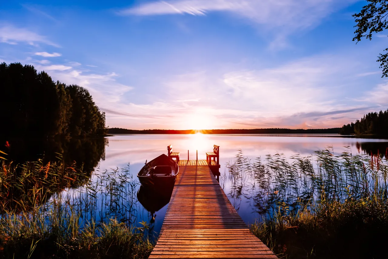 Wooden dock leading to a rowboat on a calm lake at sunset.