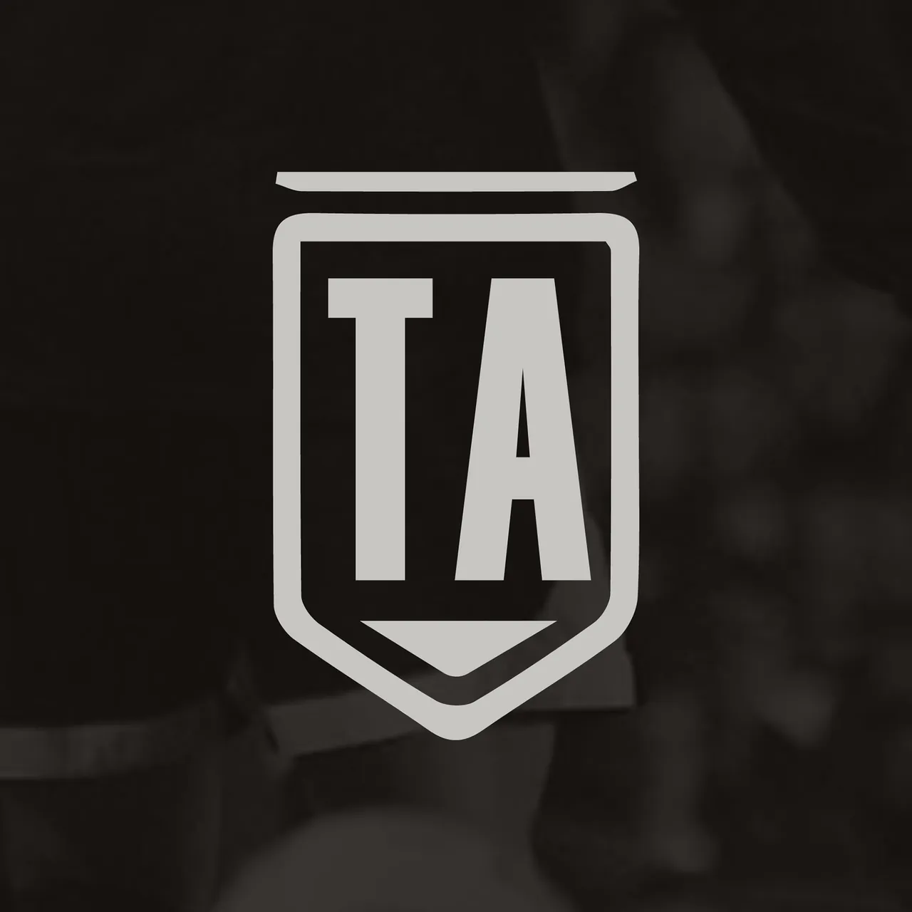 The Agenda shield monogram: the letters TA in a pennant-shield outline on a darkened match photograph.