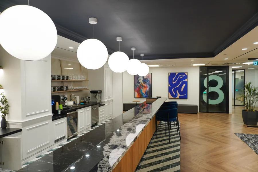 Kitchen bar with a black marble counter, large round white pendant lights, white cabinets, a blue abstract artwork and a glass door with a large number 8 in the distance.