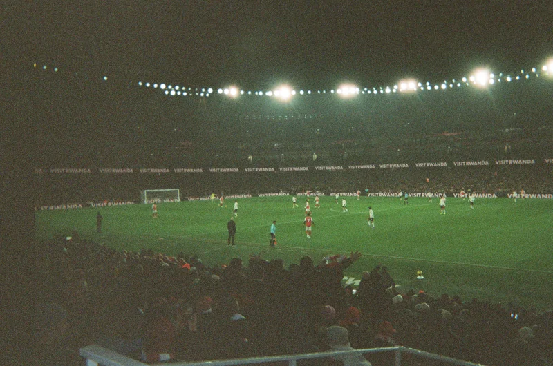 Soccer match at night under stadium floodlights, seen from the stands.